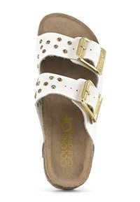 Vit sandal med två justerbara remmar, guldfärgad hårdvara och dekorativa nitar i brons och grönt. Mjuk, texturerad fotbädd för komfort.