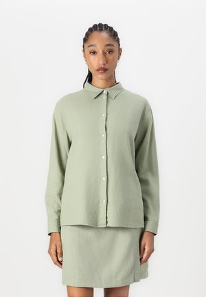 Long-sleeve, light green collared shirt with buttons, paired with a matching skirt. Soft, textured fabric with a relaxed fit.