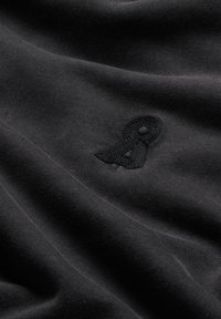 Tessuto nero con una texture morbida, caratterizzato da un logo in rilievo di un nero più scuro. Superficie liscia con leggere ondulazioni e fine rigatura.