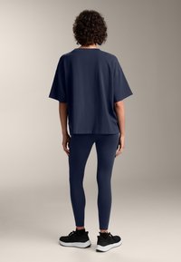 Tricou oversize bleumarin, asortat cu colanți bleumarin și încălțăminte sport neagră, văzut din spate. Material neted și croială lejeră.