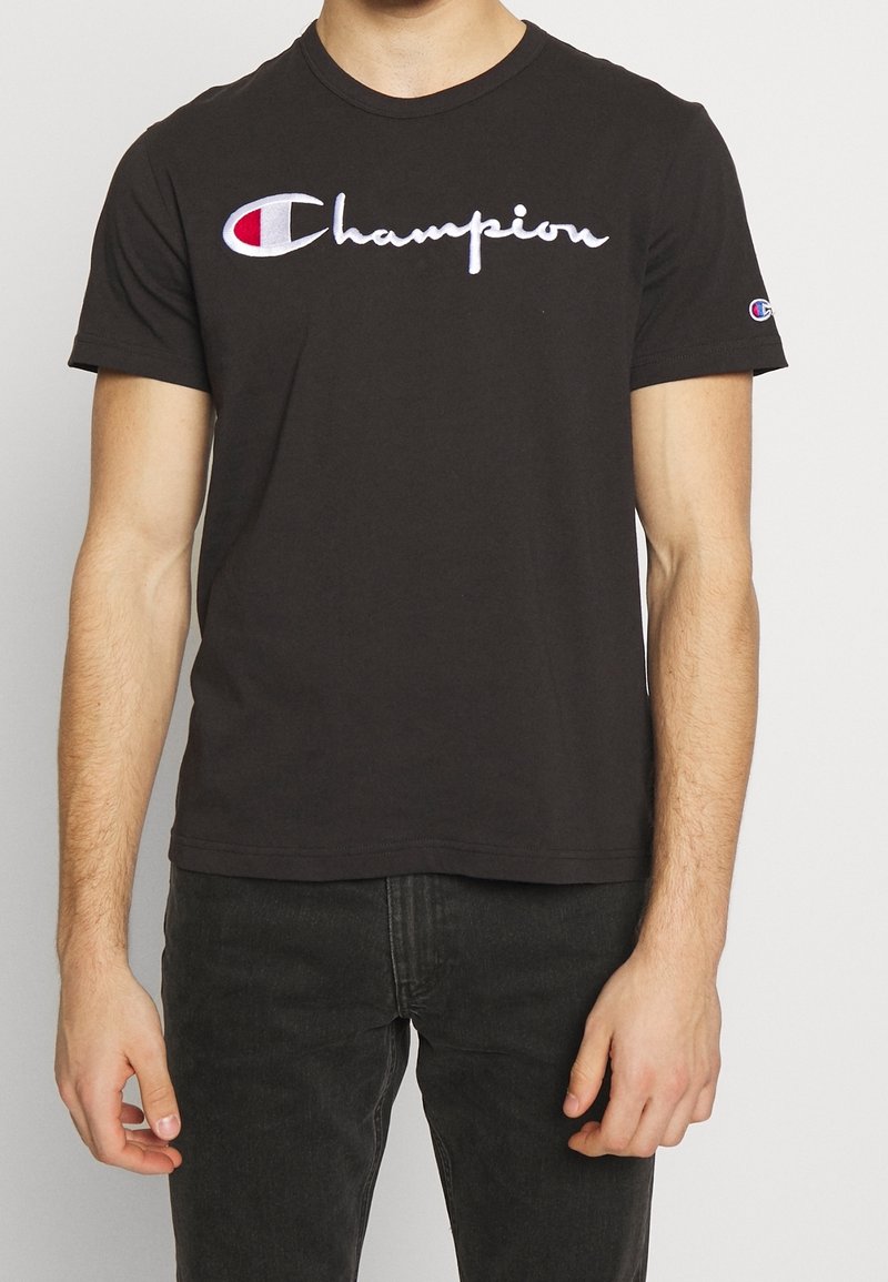 Mustat puuvillapaidat, joissa on lyhyet hihat ja pyöreä kaula-aukko, etuosassa valkoinen ja punainen kirjailtu "Champion"-logo.