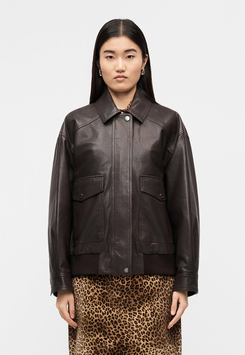 Καφέ δερμάτινο μπουφάν με γιακά, μπροστινές τσέπες και ριμπ μανσέτες. Φορεμένο πάνω από φούστα με λεοπάρ μοτίβο. Λεία υφή.