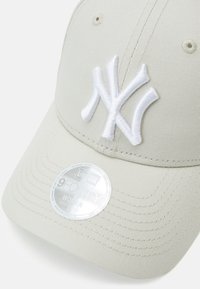 Beige színű, anyagból készült baseball sapka, hímzett fehér "NY" logóval és fényes ezüst címkével, amin az "9FORTY NŐI ÁLLÍTHATÓ" felirat található.