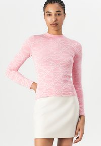 Roze langemouwtop met een gestructureerd, ingebed patroon. Gepaard met een crèmekleurige rok, wat een gelaagde outfit creëert.