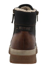 Botín de piel marrón con parte superior de textil negro, forro de lana blanca, cierre de cremallera y suela de goma gruesa. Branding "MUSTANG" exhibido.