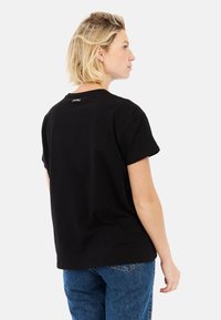 Zwarte katoenen T-shirt met korte mouwen, relaxte pasvorm, ronde halslijn en een klein logo-detail op de achterkant. De spijkerbroek is blauw en heeft een rechte snit.