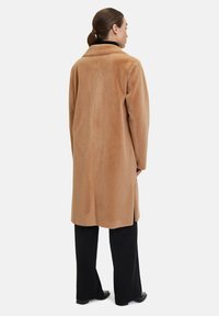 Cappotto in misto lana color sabbia con colletto alto, maniche lunghe e spacco laterale, abbinato a pantaloni neri a palazzo. Tessuto liscio e morbido.