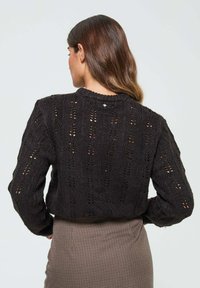 Pull en tricot noir cropped avec un design en dentelle ouverte et un col côtelé. Il a des manches longues et une coupe décontractée.