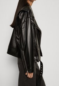 Black leather biker jacket with a slightly oversized fit, asymmetrical zipper, shoulder epaulettes, and decorative belt detail.