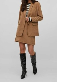 Hnědý kordový blejzr a odpovídající mini sukně v kombinaci s černobílým pruhovaným svetr a vysokými lesklými černými botami na podpatku.