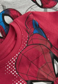 Zwei T-Shirts mit Spider-Man-Designs. Eines ist rot mit einem Grafik- und Punktemuster, das andere grau mit Spinnennetzmustern. Aus Baumwollmaterial.