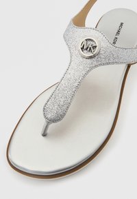 Ασημί σανδάλι σαγιονάρας με glitter, μεταλλικό λογότυπο, επίπεδη σόλα και λεία λευκή εσωτερική σόλα. Ο σχεδιασμός έχει κομψό, μίνιμαλ προφίλ.