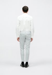 Cămașă albă cu mânecă lungă, pantaloni gri deschis, croială slim, material texturat, asortați cu pantofi negri. Vedere din spate, pe un fundal simplu.