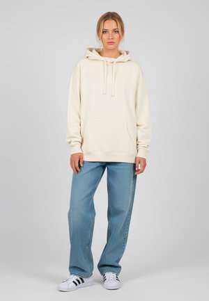 Crème hoodie met een voorzak, trekkoorden en geribbelde manchetten, gecombineerd met lichtblauwe rechte spijkerbroek en witte sneakers.