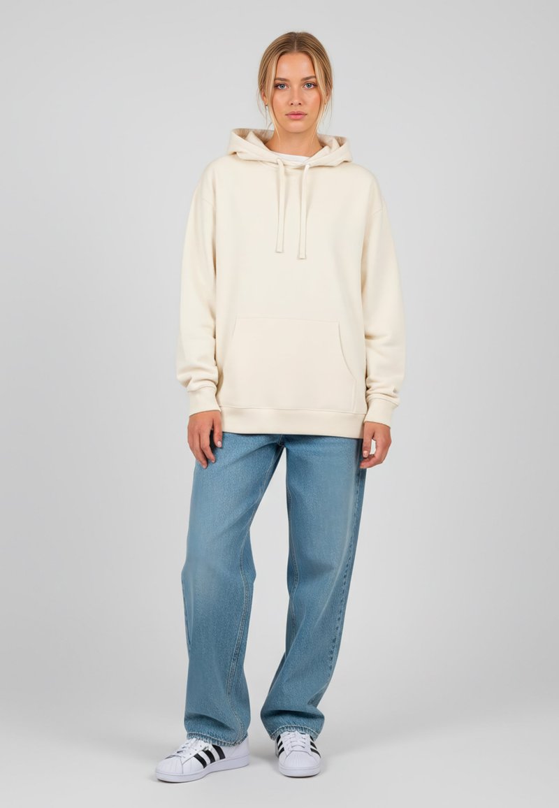 Felpa crema con tasca frontale, cordini e polsini a costine, abbinata a jeans blue chiaro a gamba dritta e sneakers bianche.
