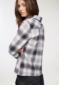 Camicia a quadri grigia e bianca con colletto, maniche lunghe, spallina posteriore e orlo curvo. Tessuto in cotone morbido con un aspetto testurizzato.
