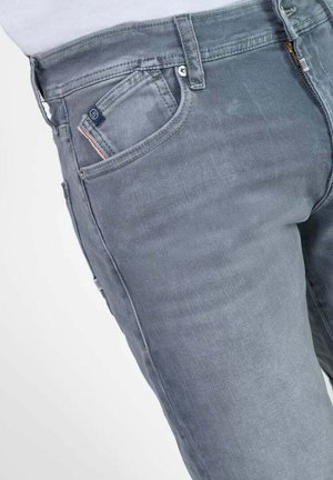 Jeans en denim gris avec une coupe slim, un design à cinq poches et des coutures contrastantes. Le matériau est lisse avec de légères variations de texture.
