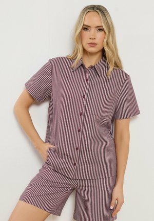 Femme debout contre un mur, portant un ensemble assorti composé d'un haut à manches courtes et d'un short à rayures verticales bordeaux et blanches.