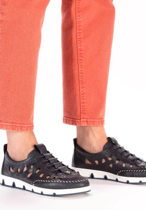 Chaussures en cuir noir avec des découpes, semelles blanches et coutures contrastées. Associées à un pantalon corail retroussé.