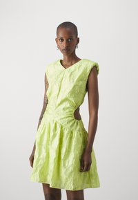 Robe vert lime avec une texture florale, manches courtes, un corsage ajusté, une découpe sur le côté et une jupe évasée. Fermeture avec un bouton à l'avant.
