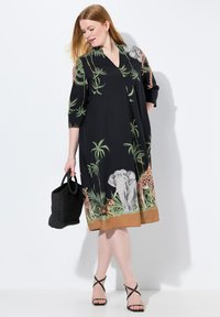 Schwarzes Kleid mit V-Ausschnitt und dreiviertel Ärmeln, verziert mit Tiermotiven eines Elefanten, einer Giraffe und eines Tigers am Saum, umgeben von grünem Blattwerk.