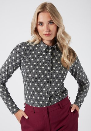 Camisa de botones a rayas en blanco y negro, con cuello y mangas largas, que presenta un diseño geométrico de líneas radiantes y puntos.