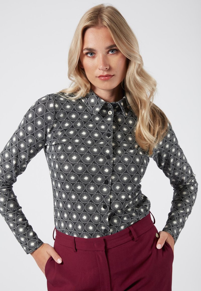Camicia a maniche lunghe a righe bianche e nere con colletto, caratterizzata da un design geometrico di linee radiali e punti.