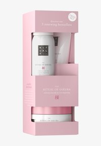 Prøvesett med tre hudpleieprodukter i hvit og rosa emballasje, med blomstermotiver og teksturerte detaljer, merket "Ritual of Sakura."