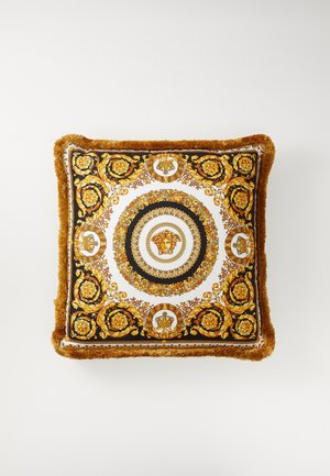 Coussin décoratif carré présentant un motif baroque or et noir, avec des bords frangés en peluche et un design de médaillon central sur un fond blanc.