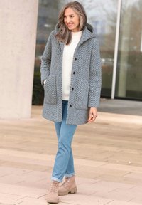 Grau gesteppter Mantel mit Kapuze, gestrickte Textur, Knopfverschluss, zwei Fronttaschen. Kombiniert mit einem cremefarbenen Pullover, hellblauen Jeans und beigen Stiefeln.