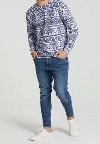 Langarmshirt met een witte achtergrond en blauwe olifanten- en geometrische patronen. Gecombineerd met slim-fit blauwe jeans en witte sneakers.