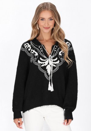 Schwarzer Pullover mit weißem besticktem Design, Quastenbänder am Ausschnitt, lockere Passform und gerippte Bündchen. Verfügt über einen strukturierten, weichen Stoff.