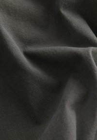 Dunkelgrauer Stoff mit einer glatten Textur, der subtile Linien und einen sanften Fall aufweist, schafft Tiefe und Dimension im Material.