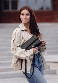 Černá kožená psaníčko s překlopnou klopou, stříbrnými detaily a nastavitelným popruhem. Nosi s béžovou bundou a světlými džíny.