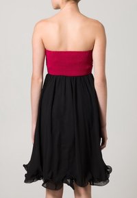 Utan axelband klänning med ett smockat överdel i stark rosa och en svävande svart kjol med ruffled nederkant.