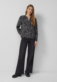 Koszula z długim rękawem, z kołnierzykiem, w ciemnoszary i czarny wzór zwierzęcy, zestawiona z czarnymi, szerokimi spodniami z wysokim stanem i błyszczącymi czarnymi butami.