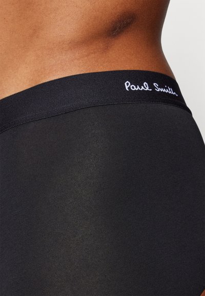 Slips noirs extensibles avec une texture lisse, présentant une taille noire brodée avec "Paul Smith" en écriture blanche.
