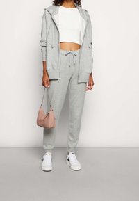 Ljusgrå bomullshuvtröja med huva och dragkedjefickor, i kombination med matchande joggingbyxor med justerbar midja och vita sneakers.