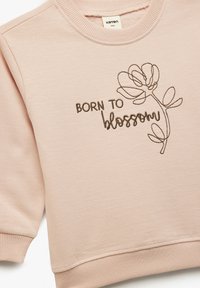 Lichtroze sweatshirt met geribbelde manchetten en halslijn. Voorzien van bruin geborduurde tekst "BORN TO blossom" en een bloemmotief. Zachte stof textuur.