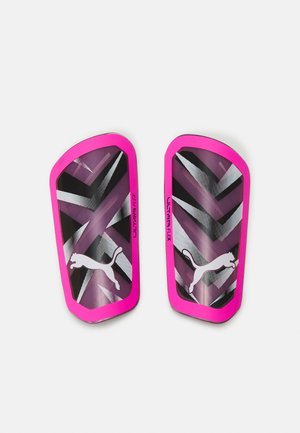 Protège-tibias Puma Ultra Flex, avec un cadre extérieur rose, un motif en chevrons noir et blanc, et un logo représentant un chat en saut.