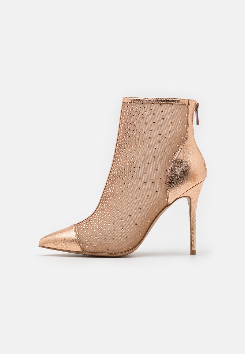 Bottine à talon haut couleur or rose, bout pointu, tige en mesh ornée de petits clous métalliques et fermeture éclair à l'arrière.