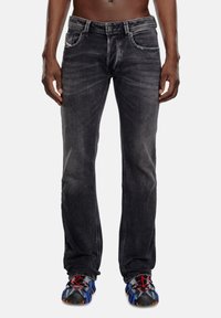 Black denim jeans featuring a slim fit, faded texture, five pockets, and contrasting stitching, paired with multicolored athletic shoes.