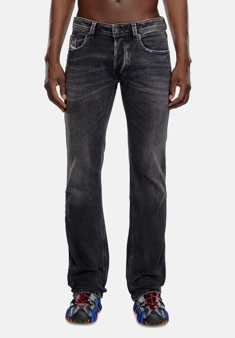 Black denim jeans featuring a slim fit, faded texture, five pockets, and contrasting stitching, paired with multicolored athletic shoes.