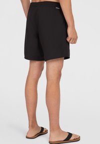 Schwarze Badeshorts mit einem elastischen Bund, glatter Textur, knielangem Schnitt und einem kleinen Logodetail auf der Rückseite. Kombiniert mit schwarzen Flip-Flops.