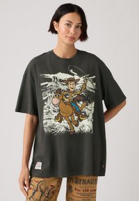 Camiseta de gran tamaño gris oscuro con un gráfico de un vaquero de dibujos animados montando un caballo. Tela de algodón, mangas cortas, diseño de cuello redondo.