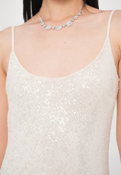 Rochie bej cu paiete, cu decolteu rotund și bretele subțiri, asortată cu un colier argintiu floral. Materialul are o textură strălucitoare.