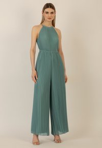 Pleated jumpsuit in teal, featuring a halter neck, elastic waistband, wide legs, and a smooth, flowing texture.