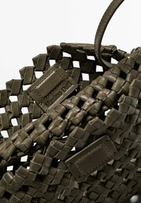 Flätad läderhandväska i olivgrön med en strukturerad yta. Visar en varumärkesetikett präglad i en rektangulär remsa. Har ett hållbart handtag.