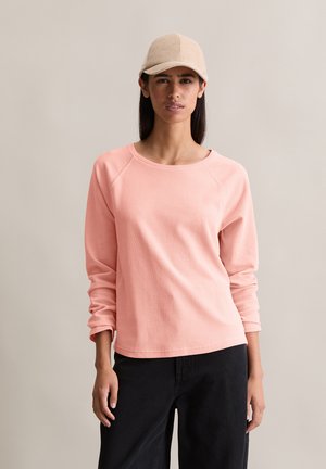 Roze longsleeve sweatshirt van een textuurstof met een ronde halslijn, gecombineerd met een zwarte broek en een beige corduroy pet.