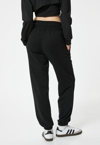 Zwarte joggingsbroek met een relaxte pasvorm, elastische tailleband en verbrede enkels. Gecombineerd met witte sneakers met zwarte accenten.